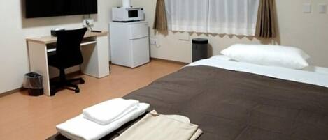 A hotel room with a bed, a desk, a chair, a television, a microwave, and a trash bin.