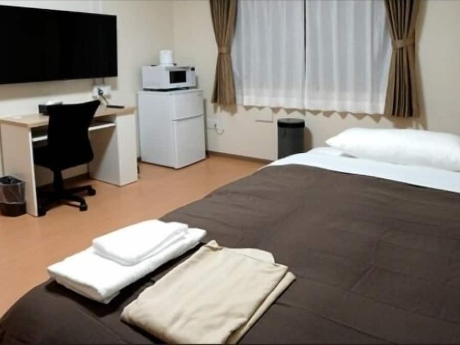 A hotel room with a bed, a desk, a chair, a television, a microwave, and a trash bin.