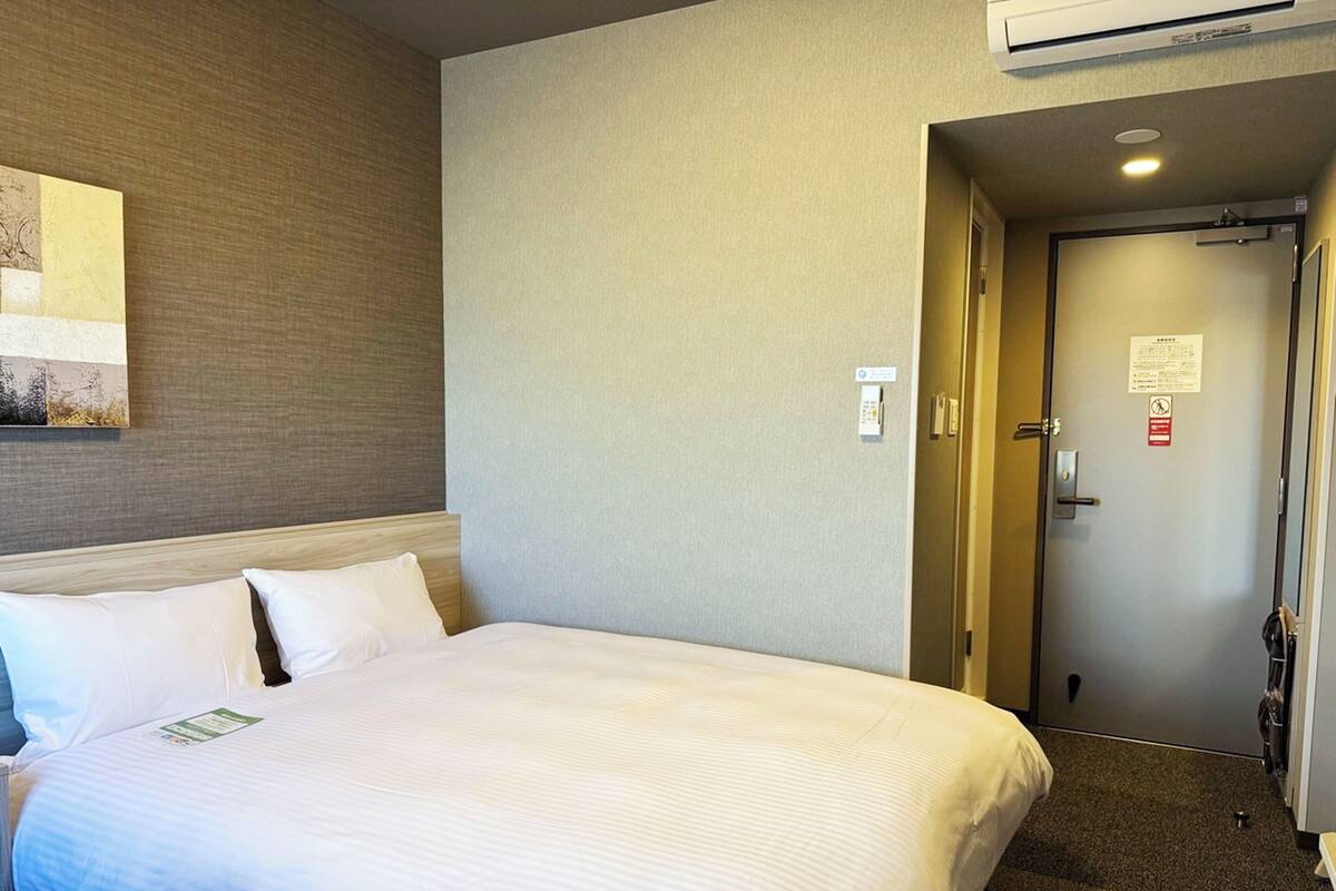 Habitación de hotel con una cama grande, cabecera, aire acondicionado de pared y una puerta que da a un baño.