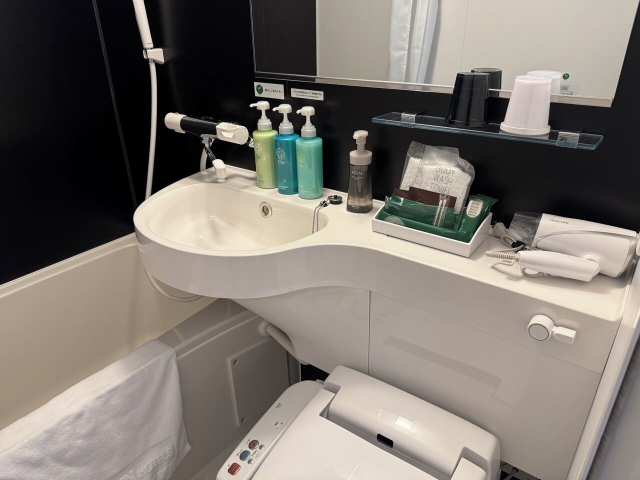 A modern bathroom with a curved sink, hand soap dispensers, a hairdryer, and a towel rack.