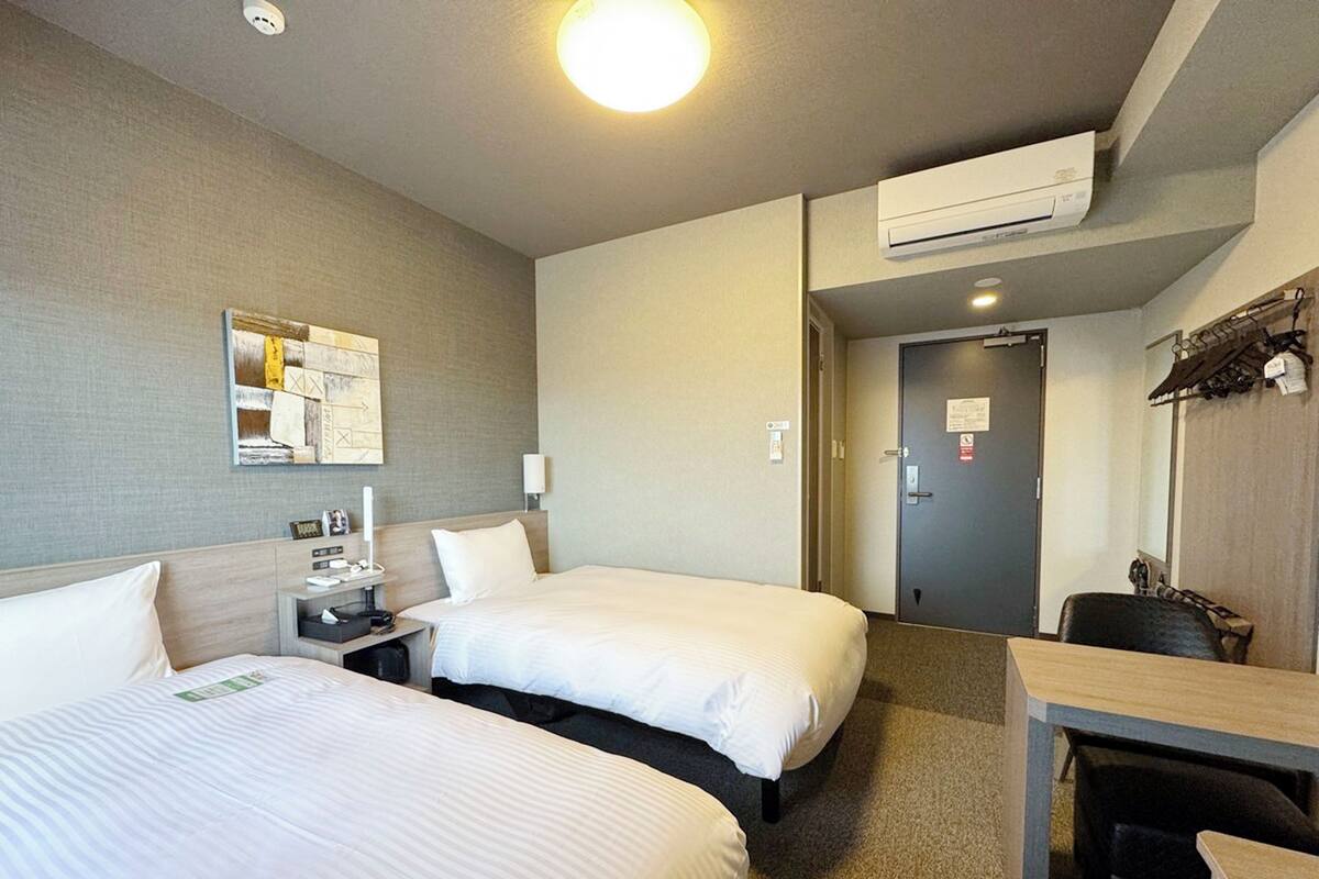 Habitación de hotel con dos camas, un escritorio, una silla, equipo de aire acondicionado y una puerta.