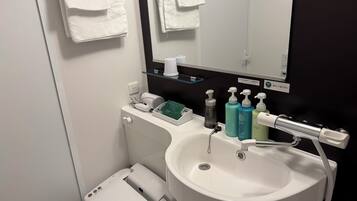 A modern bathroom with a white sink, a mirror, and a toilet. There are toiletries on the sink counter, and towels are hanging on the wall.