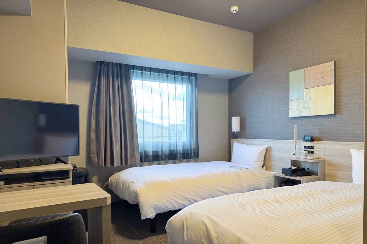 Habitación de hotel con dos camas, un escritorio, un televisor y una ventana con cortinas.