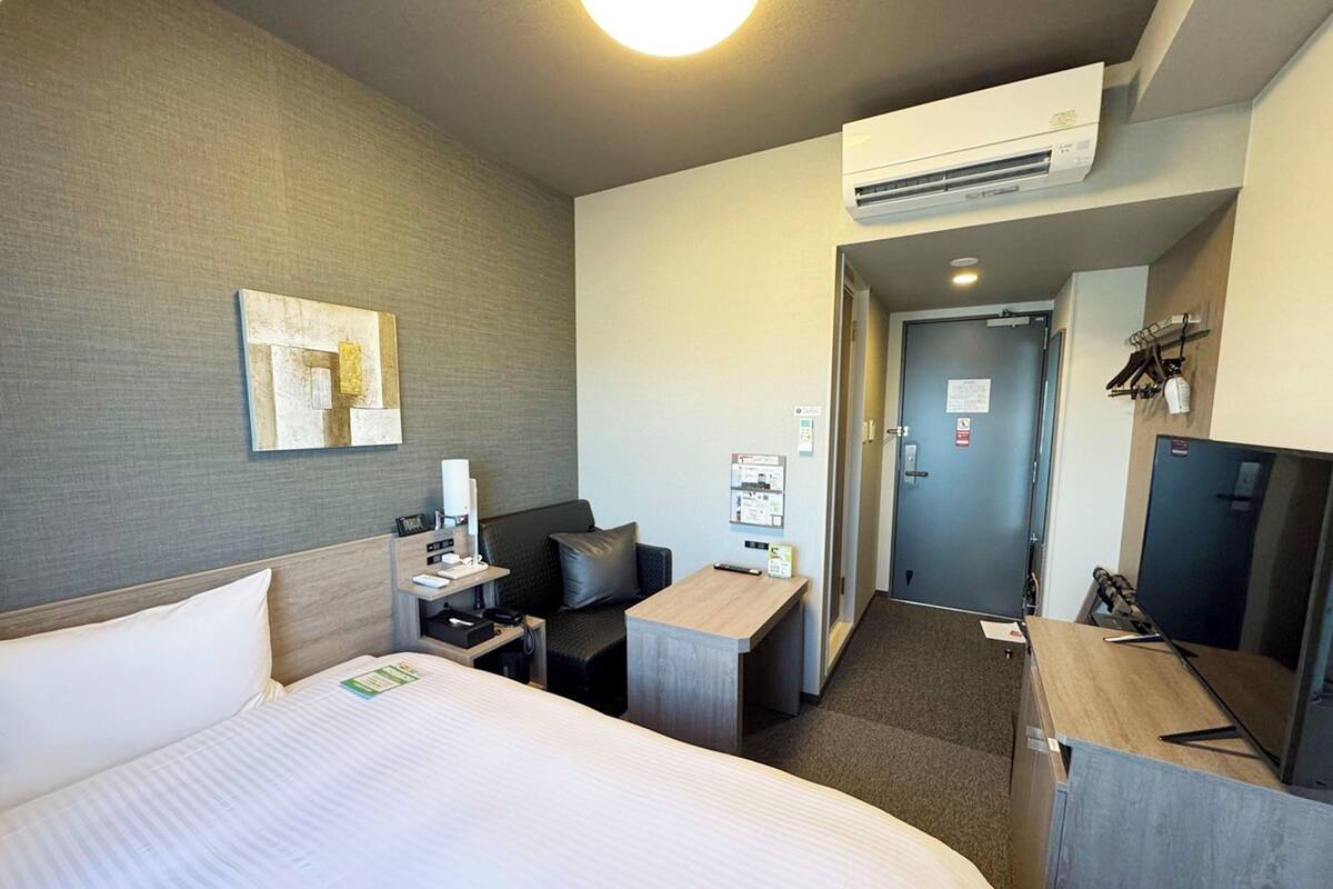 Una habitación de hotel con cama, escritorio, silla, sofá, equipo de aire acondicionado y puerta.