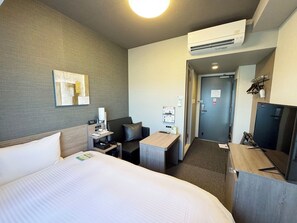 Ein Hotelzimmer mit Bett, Schreibtisch, Stuhl, Sofa, Klimaanlage und einer Tür.