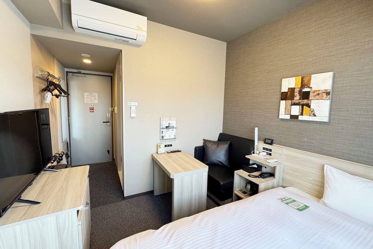 Habitación de hotel con cama, escritorio, silla, televisor y aire acondicionado.