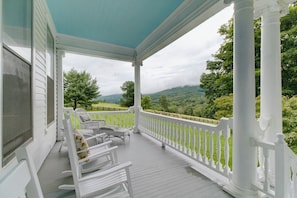 A covered porch with white railings and a view of green hills.