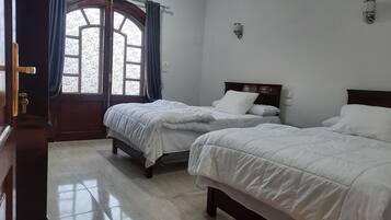 A hotel room with two beds, a wooden door, a window with curtains, and an air conditioning unit.