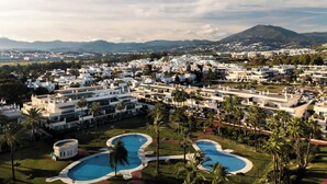 A resort with multiple buildings, a large swimming pool, and palm trees. - Locrimar | Terrace Pool View Padel Gym Apartment (Marbella)