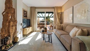 A modern living room with a large wooden sculpture, a sofa, a coffee table, and a TV. - Locrimar | Terrace Pool View Padel Gym Apartment (Marbella)