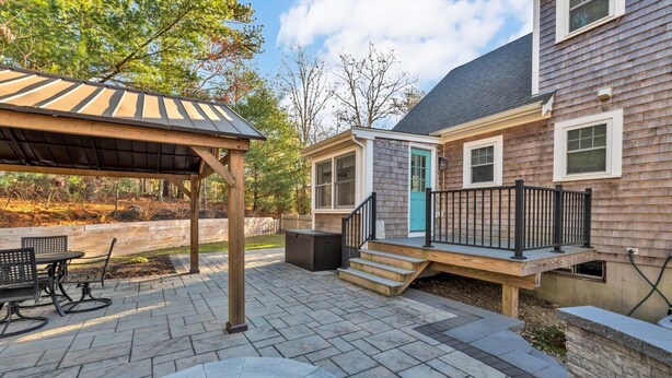 A patio area with a covered seating area, a hot tub, and a stone fire pit. - Family-Friendly Home Near Beach with Fenced Yard   |   Fire Pit, Three Bedroom Plus Office make for Four Unique Sleeping Spaces, Pocasset Home Perfect for Families, Host up to 7, 24 Hr Hospitality (Bourne)