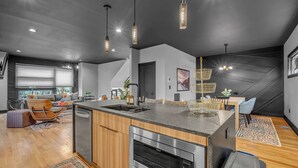 Une cuisine moderne dotée d’un îlot central, d’appareils électroménagers en acier inoxydable et de luminaires suspendus.