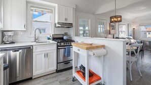 A modern kitchen with white cabinets, stainless steel appliances, and a central island with a sink and a wooden countertop.