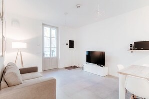 A modern living room with a sofa, a TV, a dining table, and a large window.
