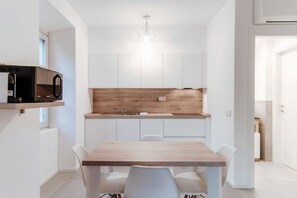 A modern kitchen with white cabinets, a wooden countertop, a built-in microwave, and a dining area with a wooden table and chairs. - Marinetti Suite 9 - MyHomeinComo (Como)