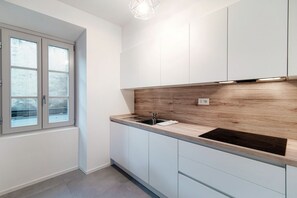 A modern kitchen with white cabinets, a wooden countertop, a black induction cooktop, and a window with frosted glass.