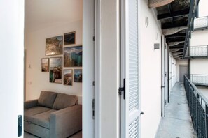 Un pasillo con sofá, decoración en la pared, una puerta con pomo y un balcón con barandilla.