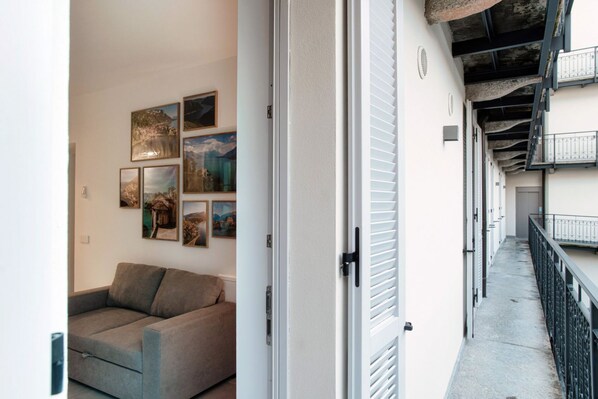 Un couloir avec un canapé et des œuvres d’art murales, une porte avec une poignée et un balcon avec des balustrades.