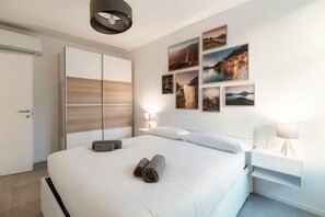 A modern hotel room with a large bed, a wardrobe, a bedside table with a lamp, and wall art. - Marinetti Suite 9 - MyHomeinComo (Como)