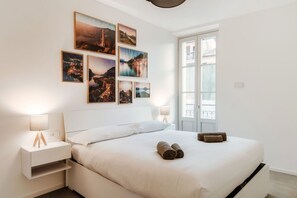Une chambre à coucher avec un lit, des tables de chevet, des tableaux accrochés au mur et une fenêtre.
