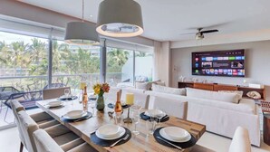 A modern dining area with a wooden table set for six, a white sofa, and a television displaying a menu.