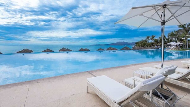 A poolside area with lounge chairs and umbrellas, overlooking a clear blue pool and a tropical beach setting. - Peninsula Deluxe Resort, 4 BR, Great Ocean Views, Great amenities (Flamingos)