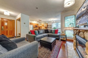 A living room with a sectional sofa, ottoman, and a fireplace. - Greystone Lodge 224 Ski-in/Out by Acer Vacations (Whistler)