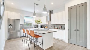 Una cocina moderna con armarios blancos, electrodomésticos de acero inoxidable y una isla central con taburetes de bar.