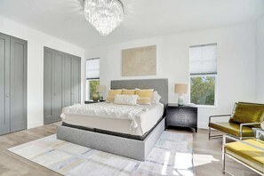 A bedroom with a bed, bedside tables, a chair, a chandelier, and a window.