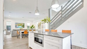 Una cocina moderna con una isla central, un comedor con mesa y sillas, y una escalera.