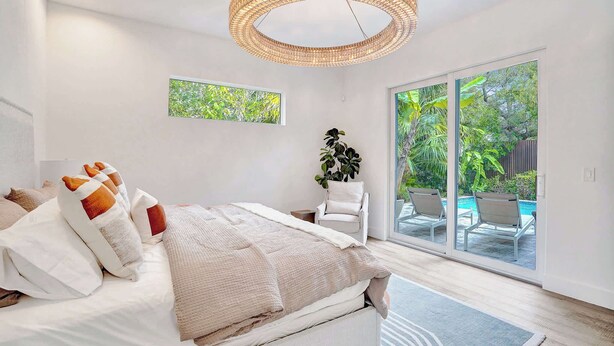 Un dormitorio con una cama grande, una lámpara de techo circular, vistas a una piscina a través de puertas de cristal y una planta en maceta.