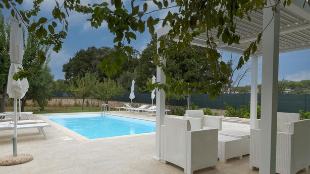 Un'area esterna coperta con piscina, mobili in vimini bianco e ombrelloni.