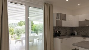 Una cucina moderna con mobili bianchi e un piano di lavoro grigio, e una porta scorrevole in vetro che dà su un balcone esterno con arredi bianchi.