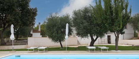 A swimming pool with lounge chairs and umbrellas, surrounded by trees and a building.