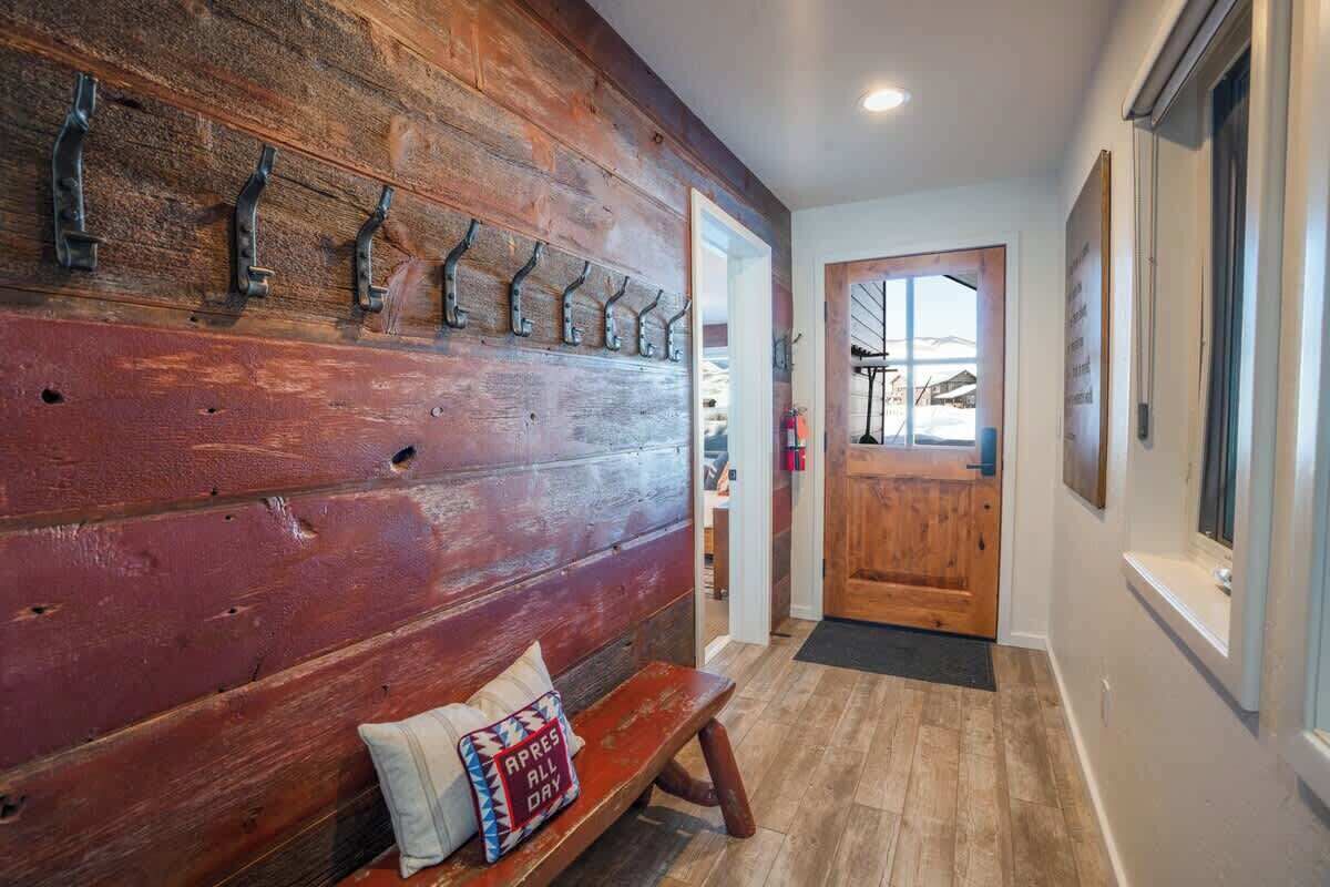 A wooden wall with hooks, a bench with a pillow, and a wooden door.