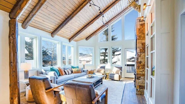 A spacious living room with a high ceiling, large windows, and a stone wall.