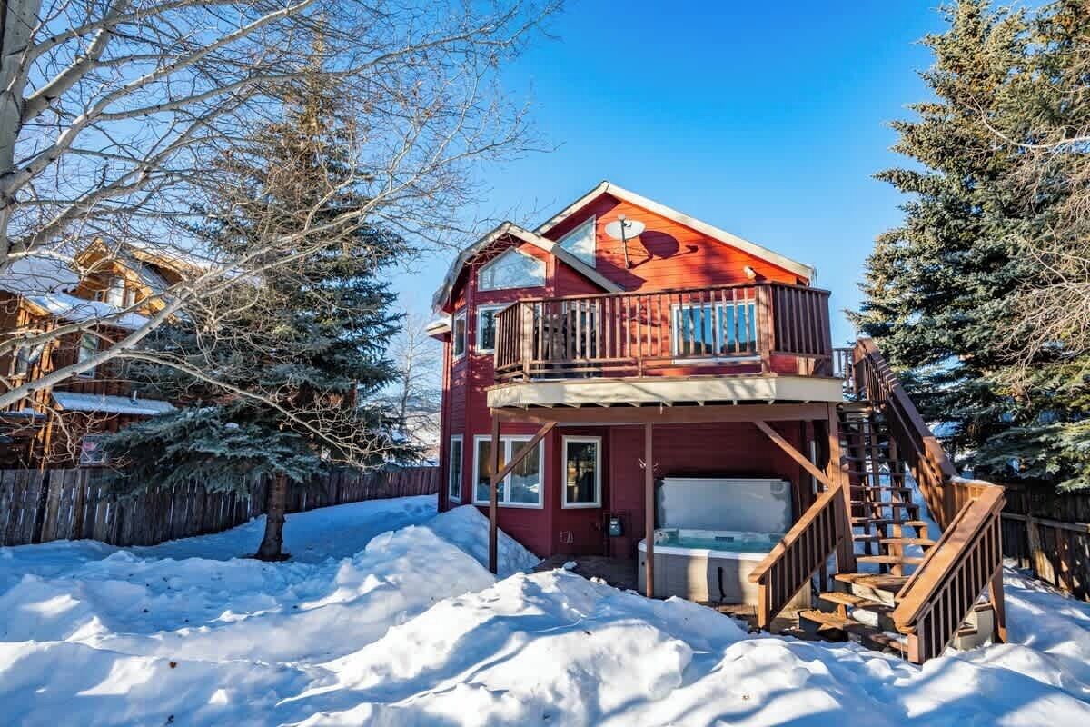 A two-story wooden cabin with a balcony, a hot tub, and a wooden staircase.
