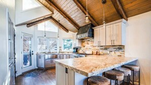 A kitchen with a large island, wooden ceiling beams, and a view of the outdoors.