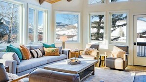 A cozy living room with a fireplace, large windows, and a view of snowy mountains.