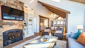 A spacious living area with a stone fireplace, a flat-screen TV, and a herringbone-patterned floor.