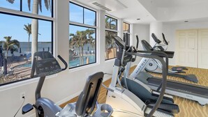 Une salle de sport équipée de tapis de course, d’un appareil elliptique et offrant une vue sur la piscine.