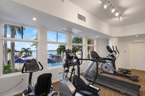 Ein Fitnessraum mit Cardiogeräten, großen Fenstern und Blick auf einen Pool und Palmen.