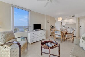 A living room with a sofa, a coffee table, a TV, and a dining area with chairs and a table. - Painted Skies, Estero Bay & Pool Views | Extended Balcony | Pool & Hot Tub | Lovers Key Resort (Fort Myers Beach)