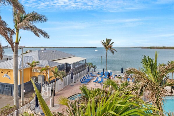 A resort with a pool area, palm trees, and a view of the water. - Painted Skies, Estero Bay & Pool Views | Extended Balcony | Pool & Hot Tub | Lovers Key Resort (Fort Myers Beach)
