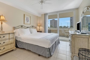 A hotel bedroom with a bed, bedside tables, a dresser, a television, and a balcony with a view of buildings. - BAY & POOL VIEWS | EXTENDED BALCONY | FREE PARKING & WIFI | KEYLESS ENTRY | LOVERS KEY RESORT (Fort Myers Beach)