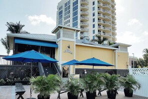 Ein Hotel mit blauer Markise, Außenbereich mit Sonnenschirmen und einem hohen Gebäude im Hintergrund.