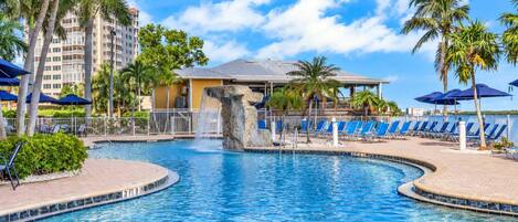 A swimming pool with a waterfall feature, surrounded by lounge chairs and palm trees.