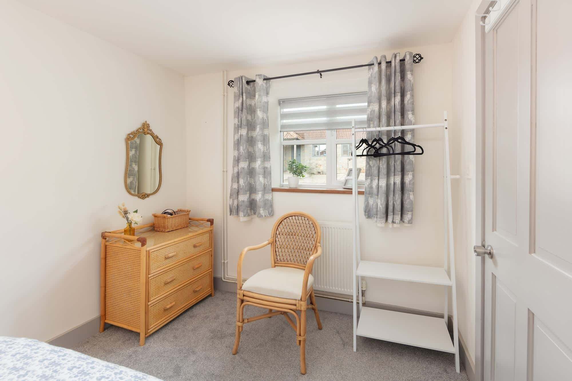 A bedroom with a bed, a dresser, a chair, a radiator, a window with curtains, and a door.