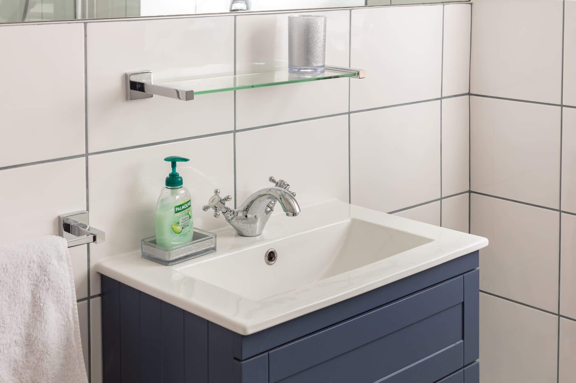 A bathroom with a white sink, a mirror, and a soap dispenser.