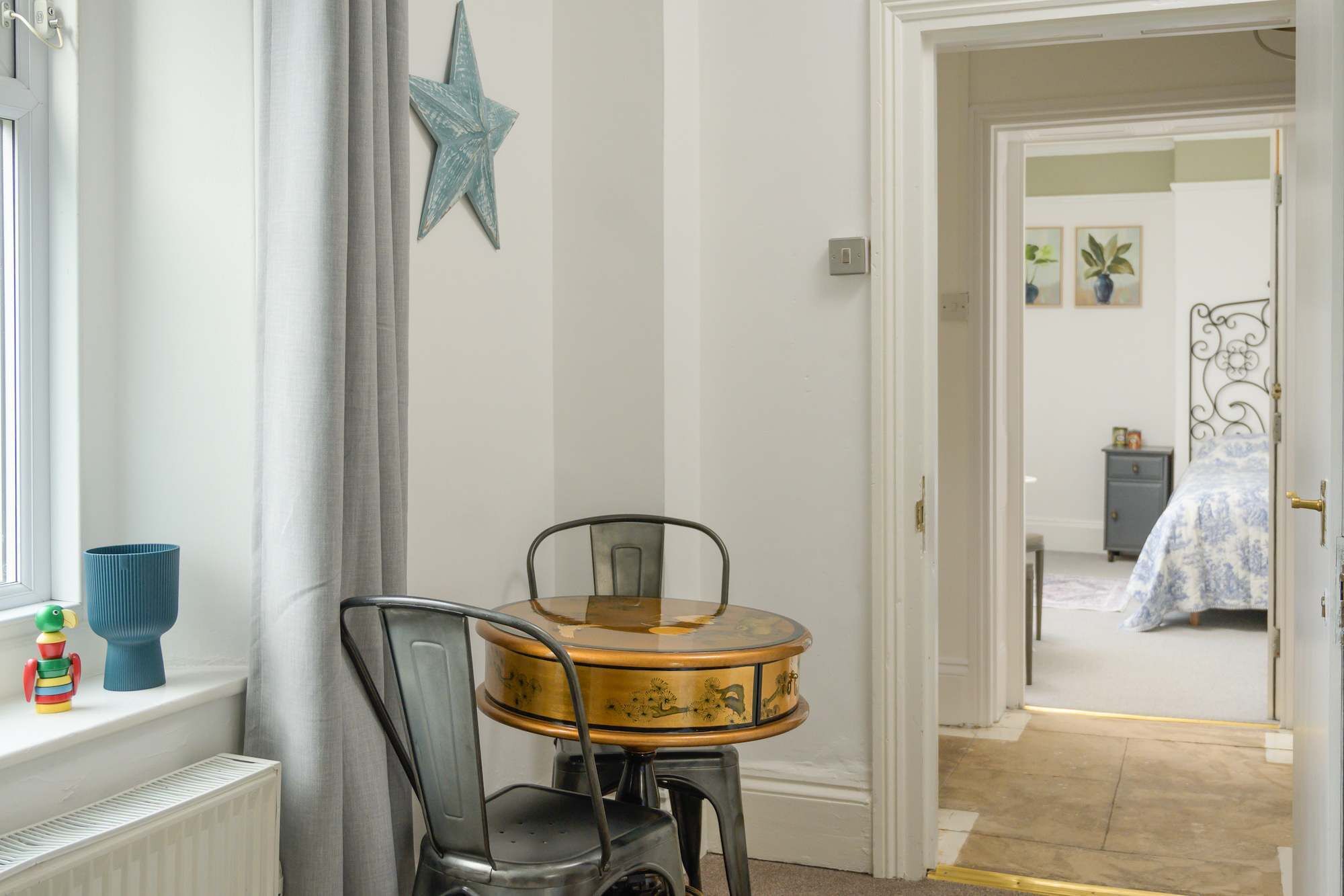 A room with a round table, a chair, a star decoration, a radiator, and a door leading to another room.